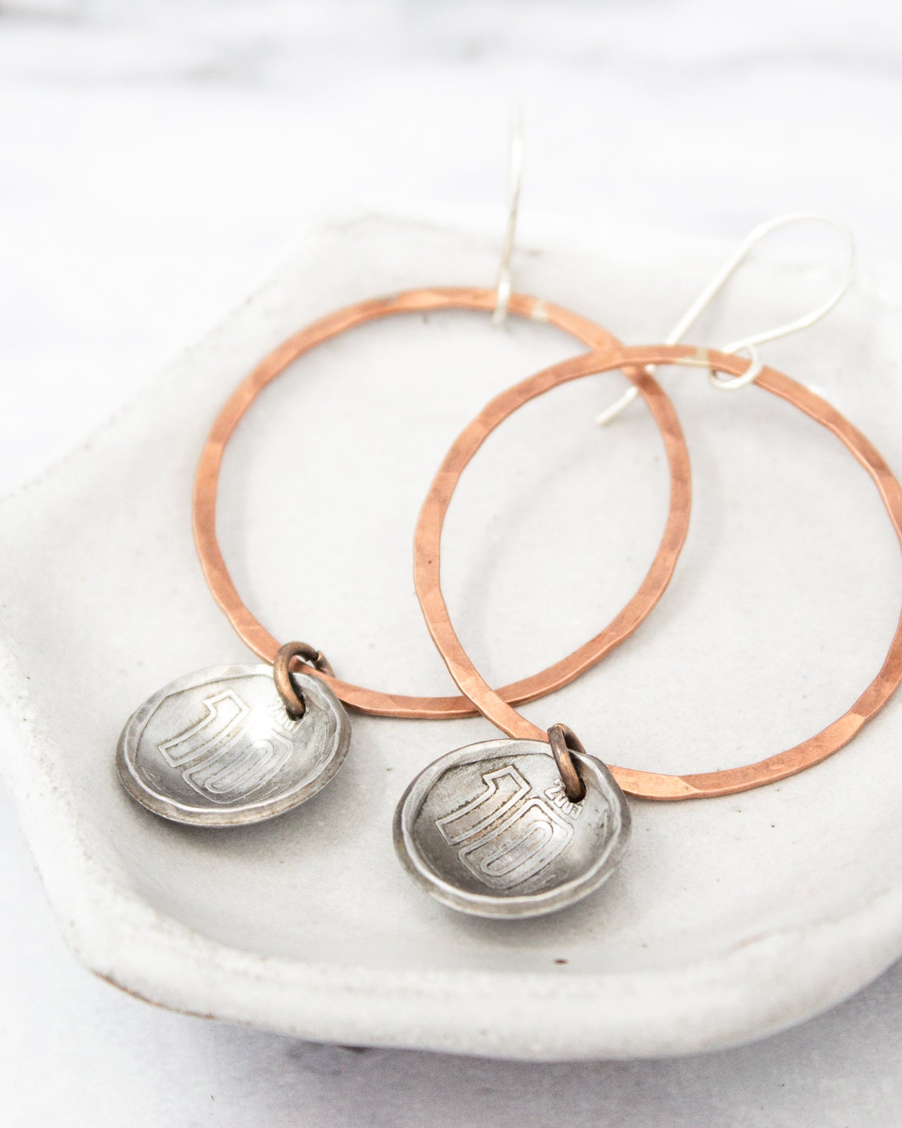 A pair of earrings with a copper-colored metal frame and silver-colored metal pendants, resting on a white surface.