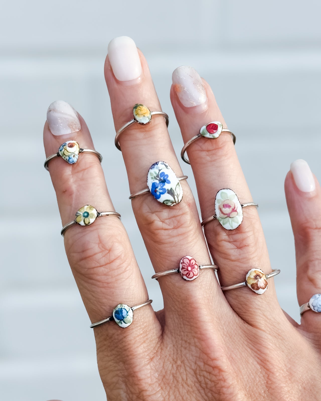 A close-up of a person's hand wearing multiple rings on each finger, each ring featuring a unique design.