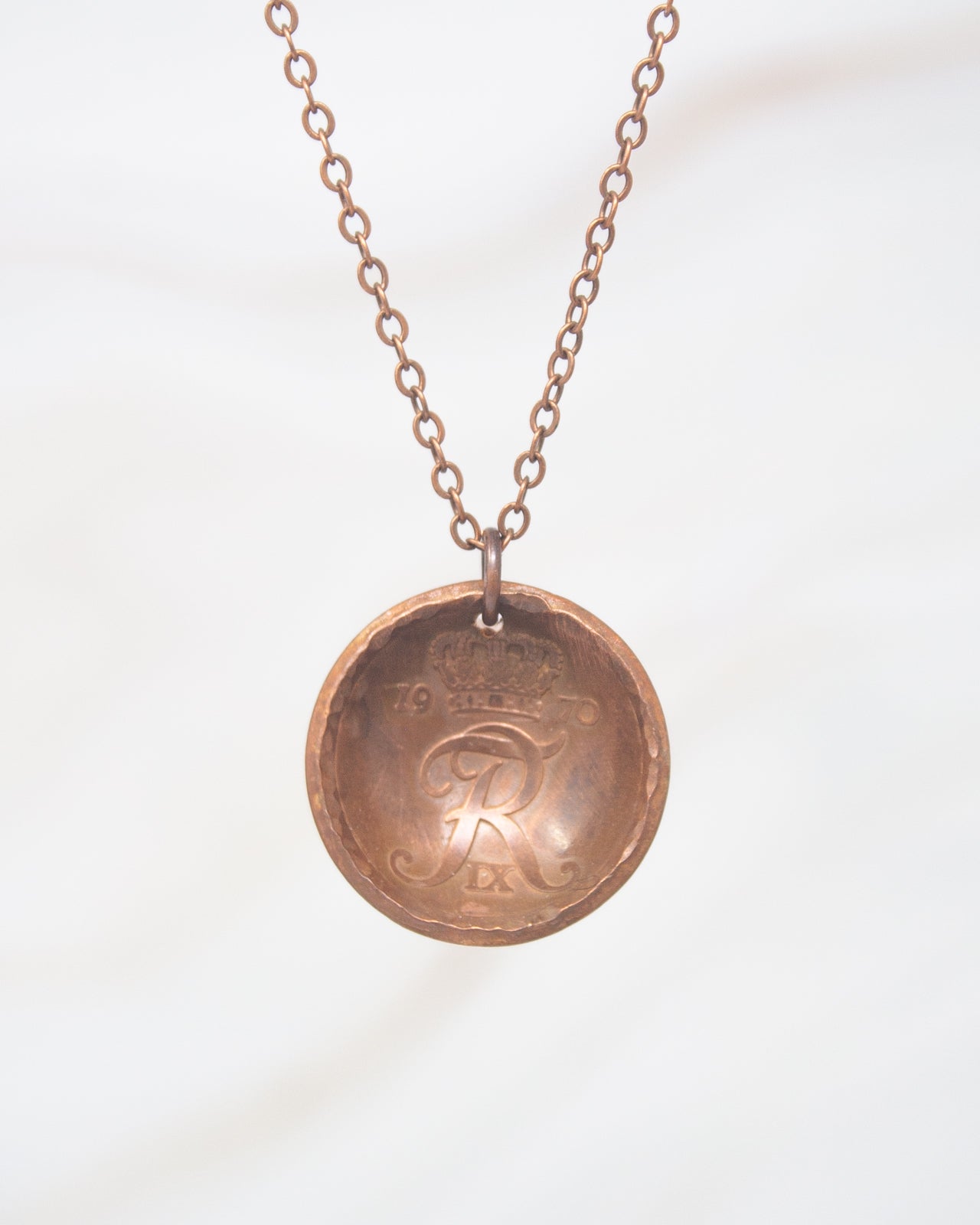 A copper-colored pendant necklace with a circular design featuring a letter "R" inside it.