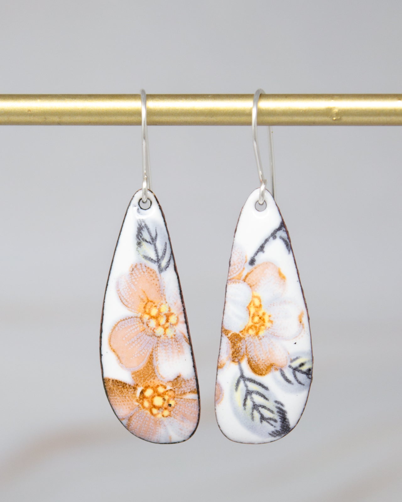 A pair of earrings with a floral design, hanging from a gold-colored metal hook.