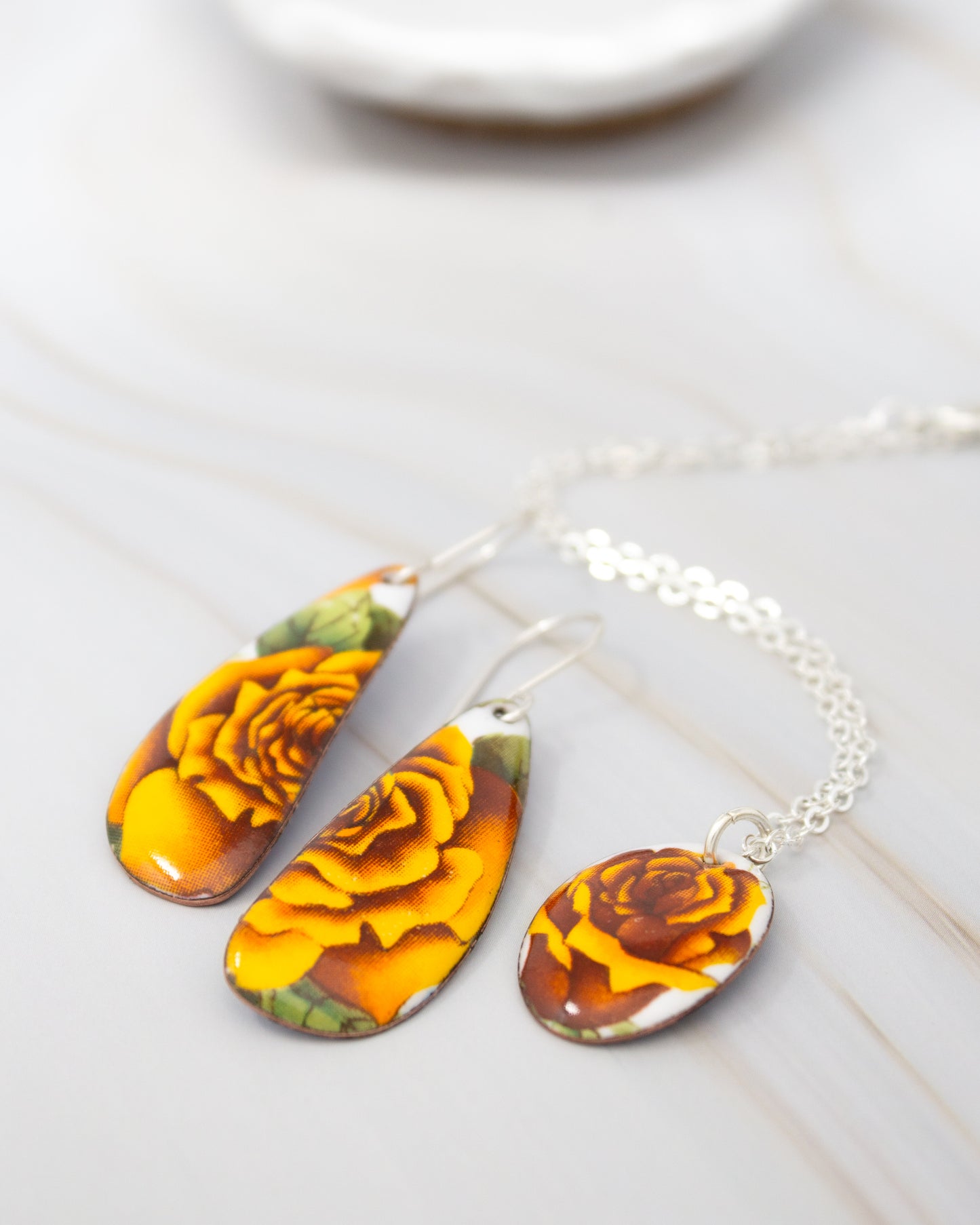A pair of earrings and a necklace with yellow and orange floral designs are displayed on a white surface.