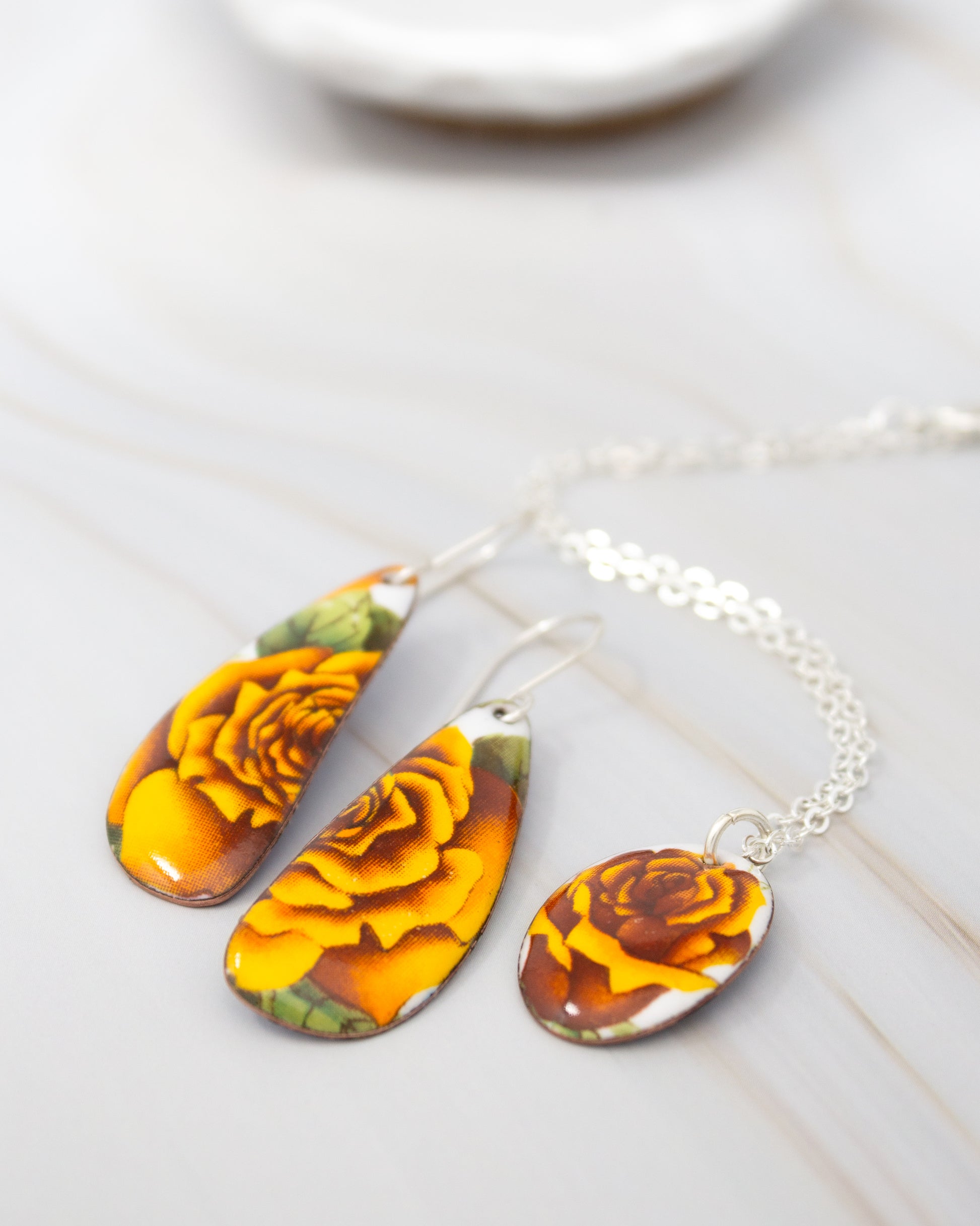 A pair of earrings and a necklace with yellow and orange floral designs are displayed on a white surface.