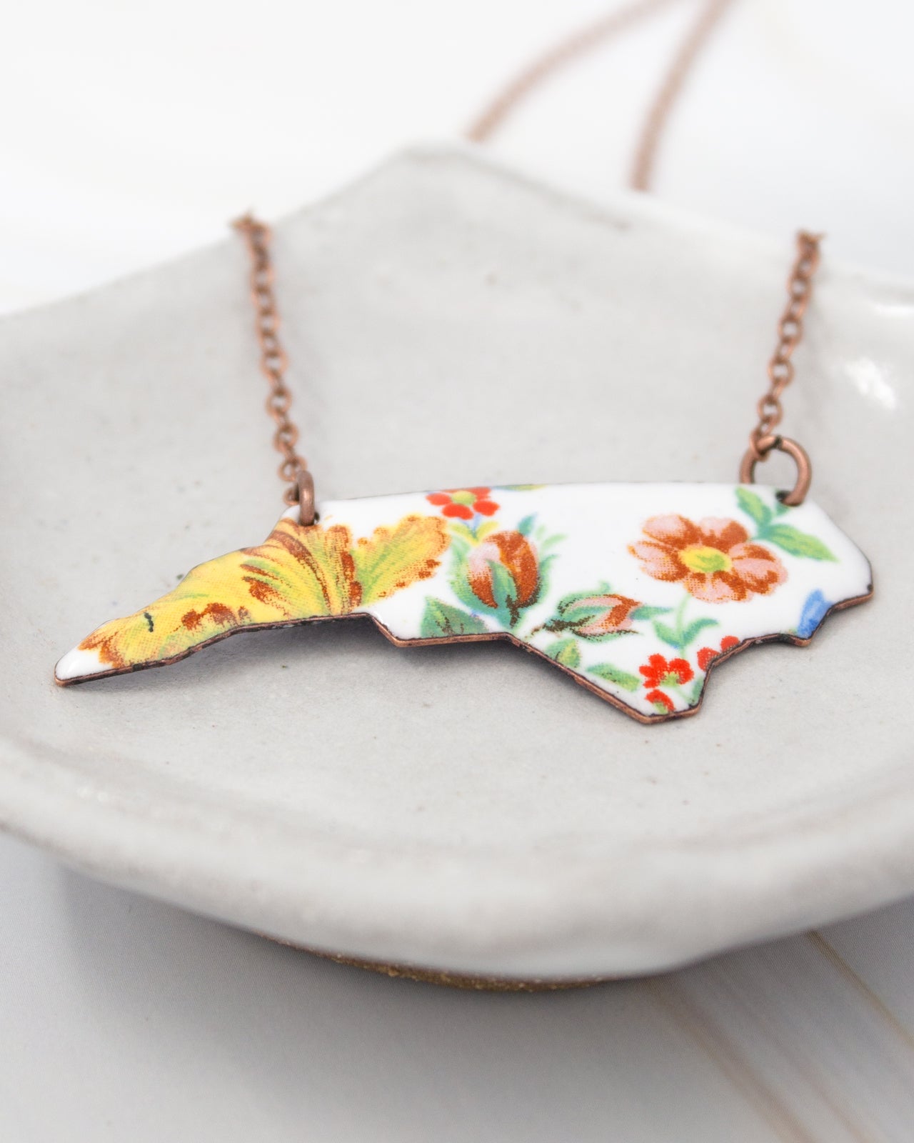A necklace with a pendant in the shape of the state of North Carolina, featuring a floral design.