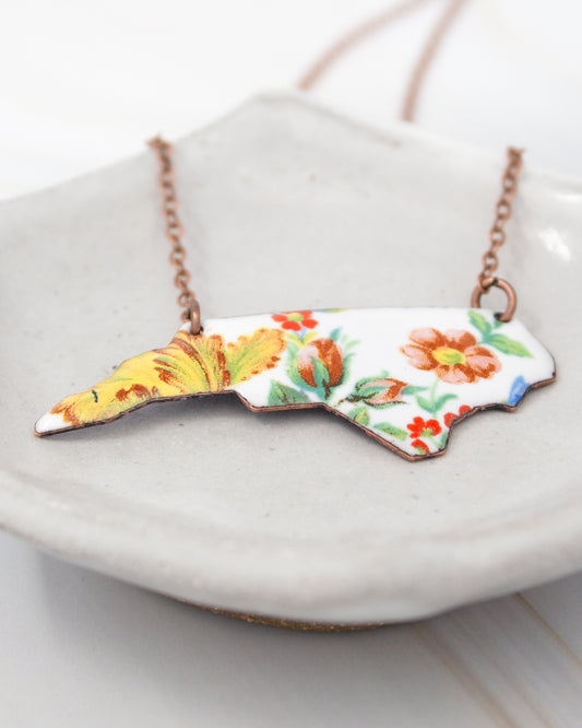 A necklace with a pendant in the shape of the state of North Carolina, featuring a floral design.