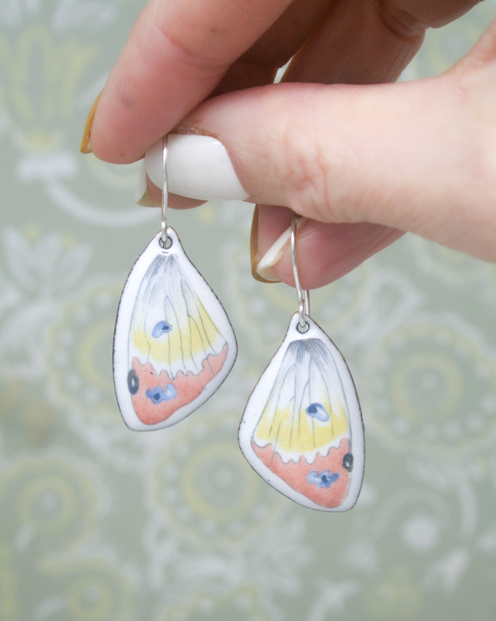 A hand holding a pair of earrings with butterfly wing designs.