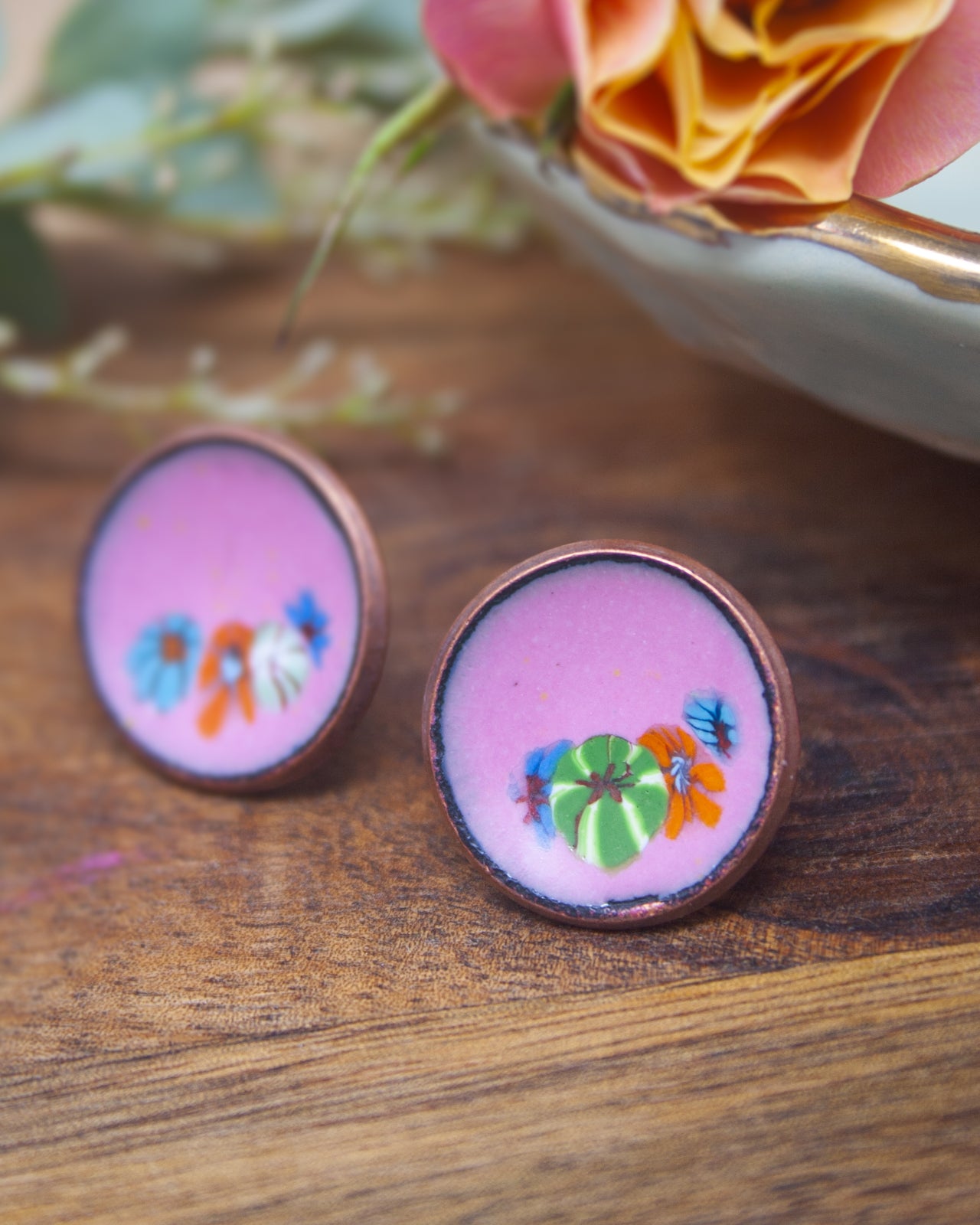 two round earrings with a floral design, placed on a wooden surface.