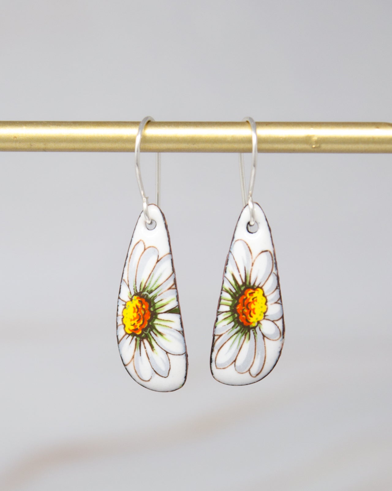A pair of white earrings with yellow and green flower designs hanging from a gold bar.