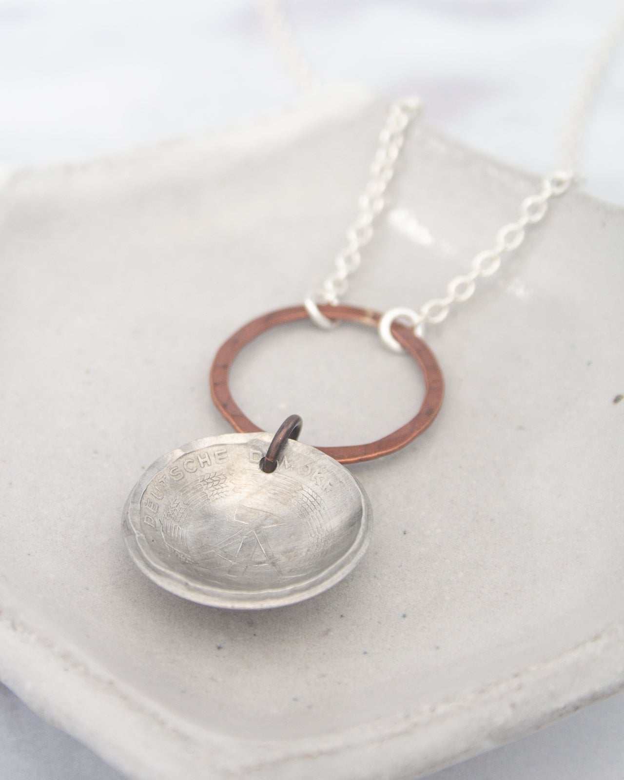 A silver necklace with a circular pendant featuring a textured design, resting on a white surface.