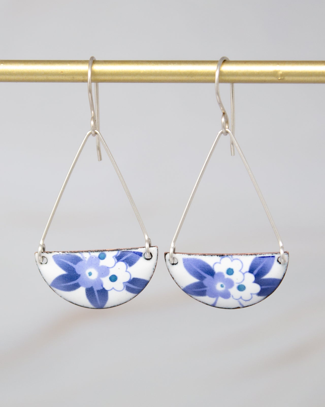 A pair of silver earrings with blue floral designs hanging from a gold bar.
