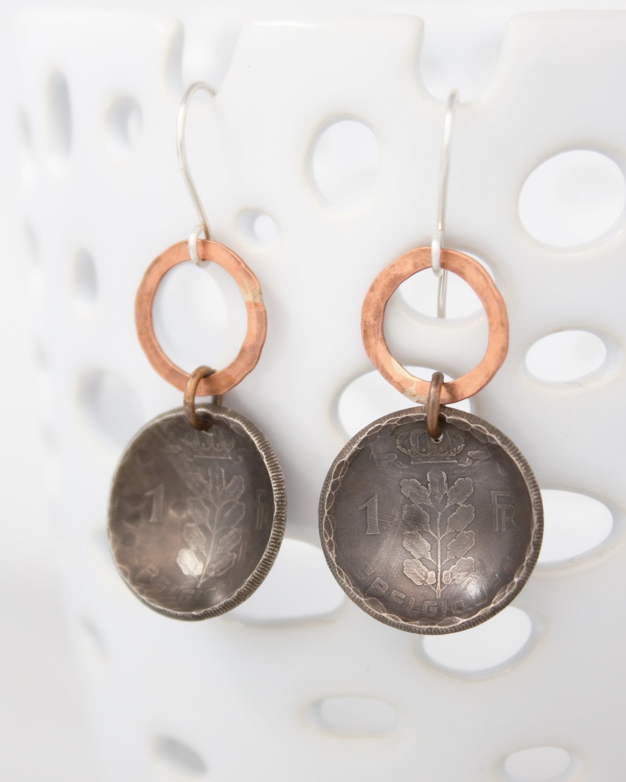 A pair of earrings made from two old coins, featuring a tree design on the surface.