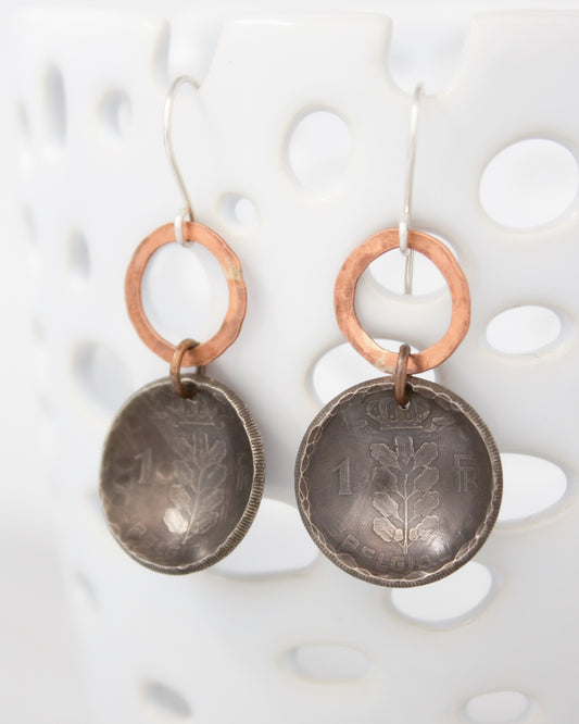 A pair of earrings made from two old coins, featuring a tree design on the surface.