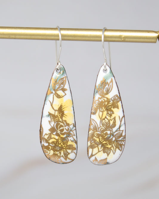 A pair of earrings with a floral design, featuring yellow and green leaves on a white background.
