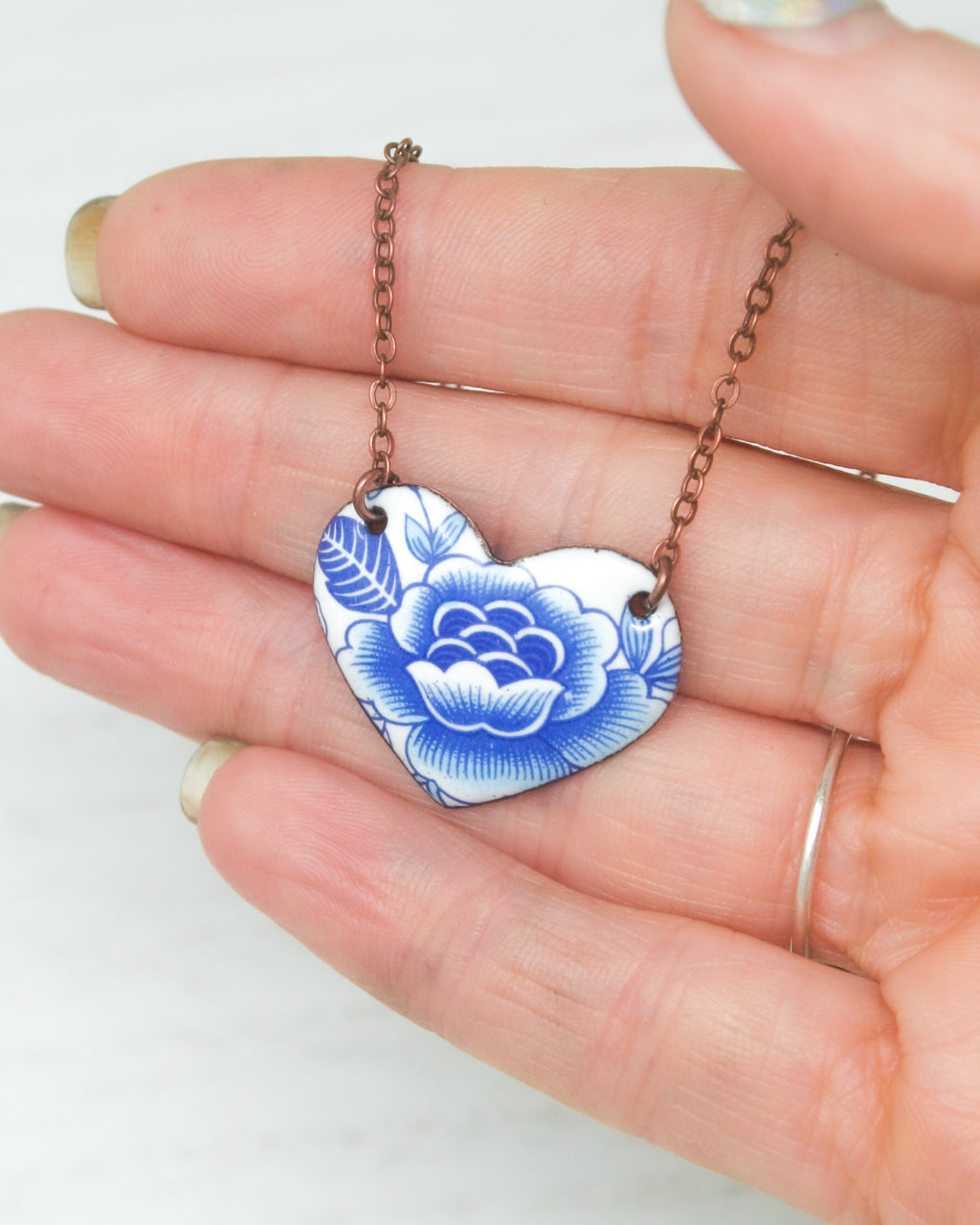 a hand holding a blue and white heart shaped necklace