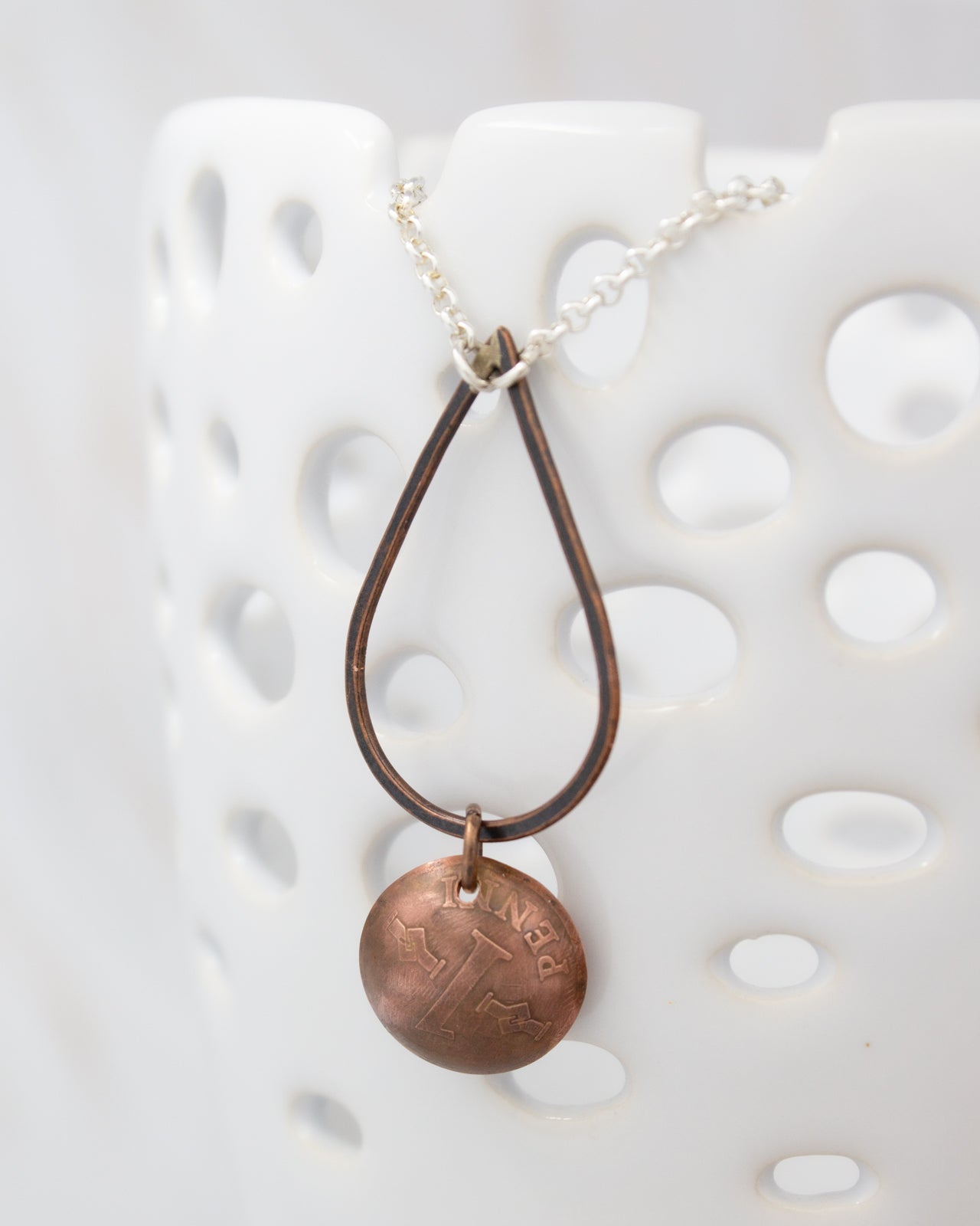 A necklace with a round metal pendant featuring an embossed design, hanging from a chain against a white background.