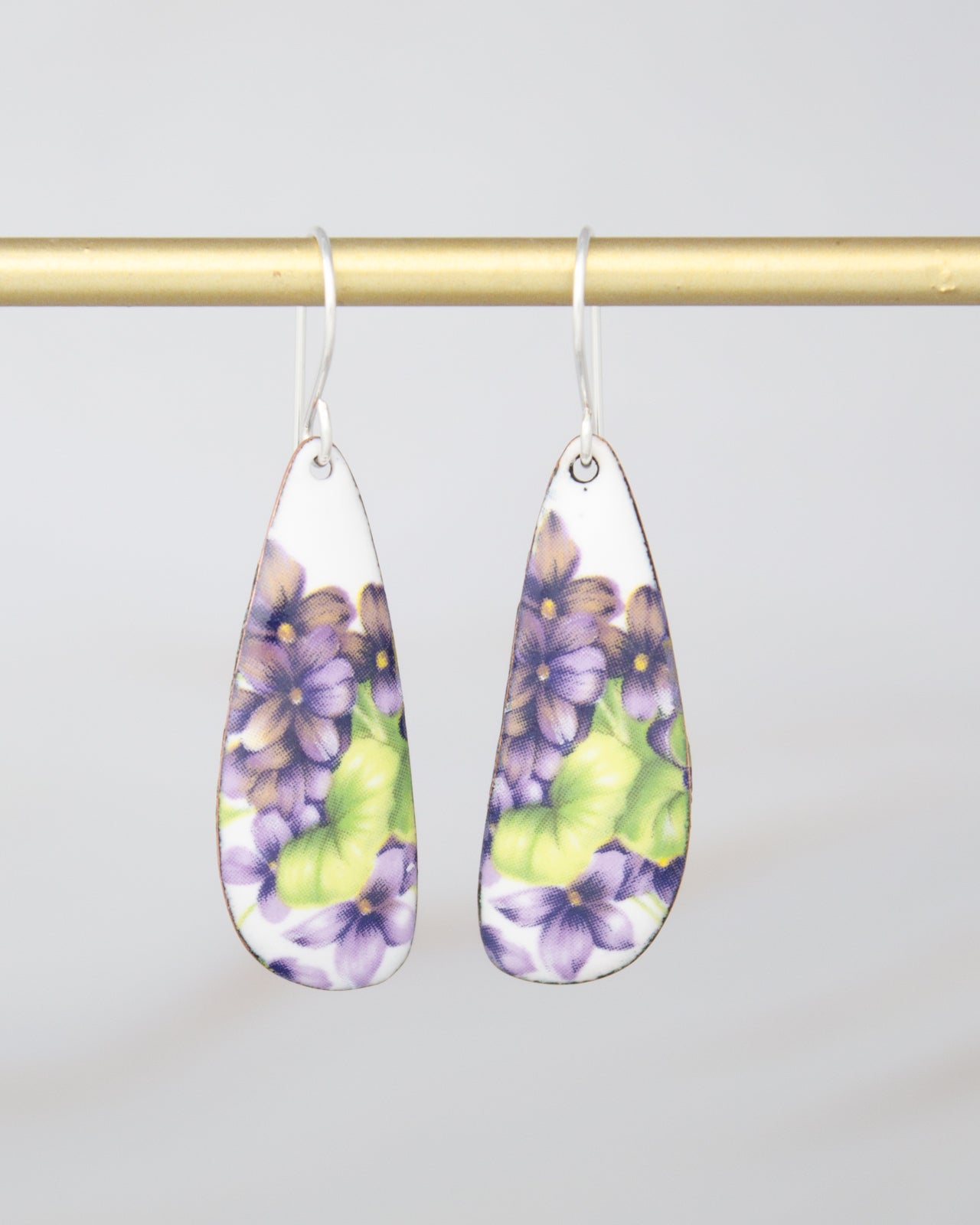 A pair of earrings with a floral design, featuring purple and green flowers on a white background.