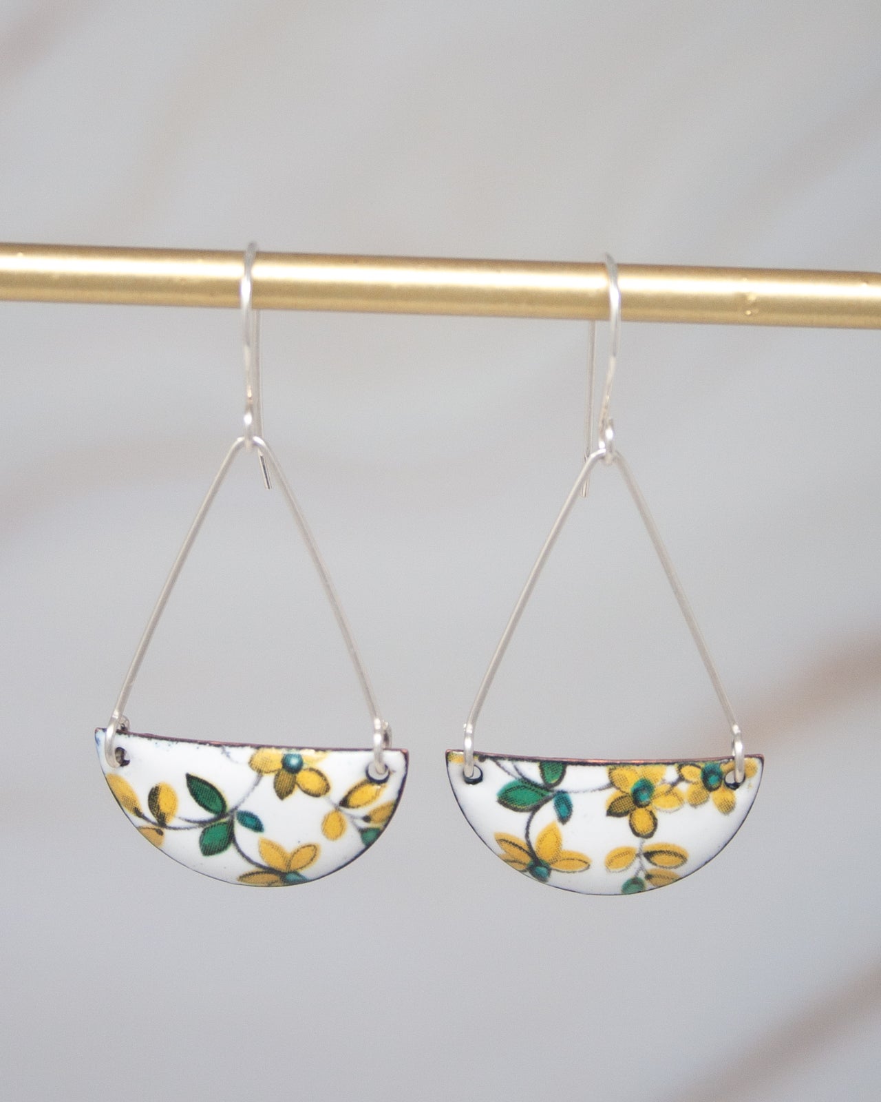 A pair of earrings with a floral design hanging from a gold-colored metal hook.