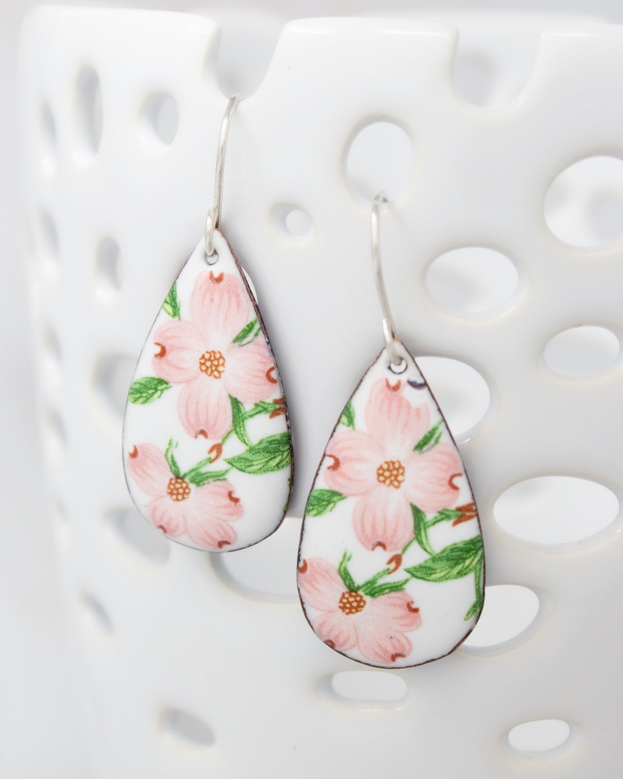 A pair of earrings with a floral design, featuring pink flowers and green leaves.