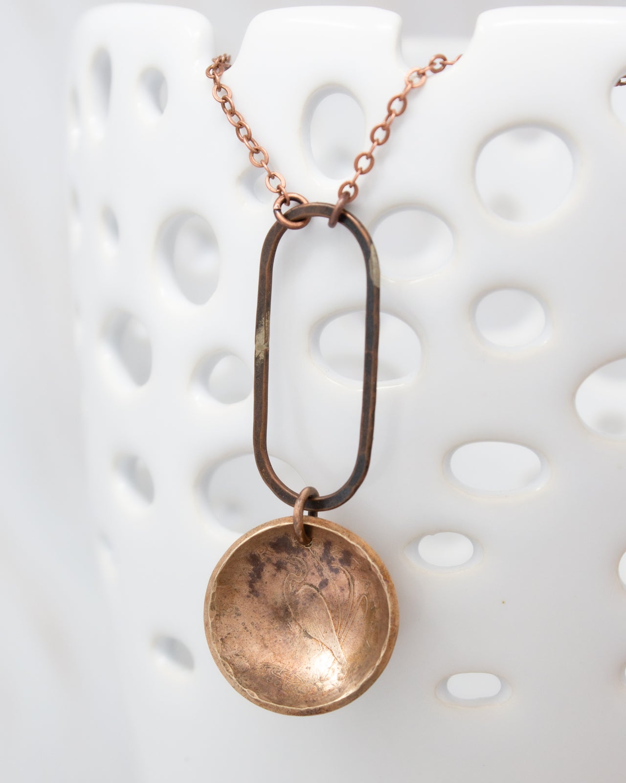 A necklace with a circular pendant and a metal frame hanging from it.