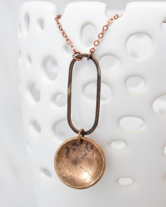 A necklace with a circular pendant and a metal frame hanging from it.