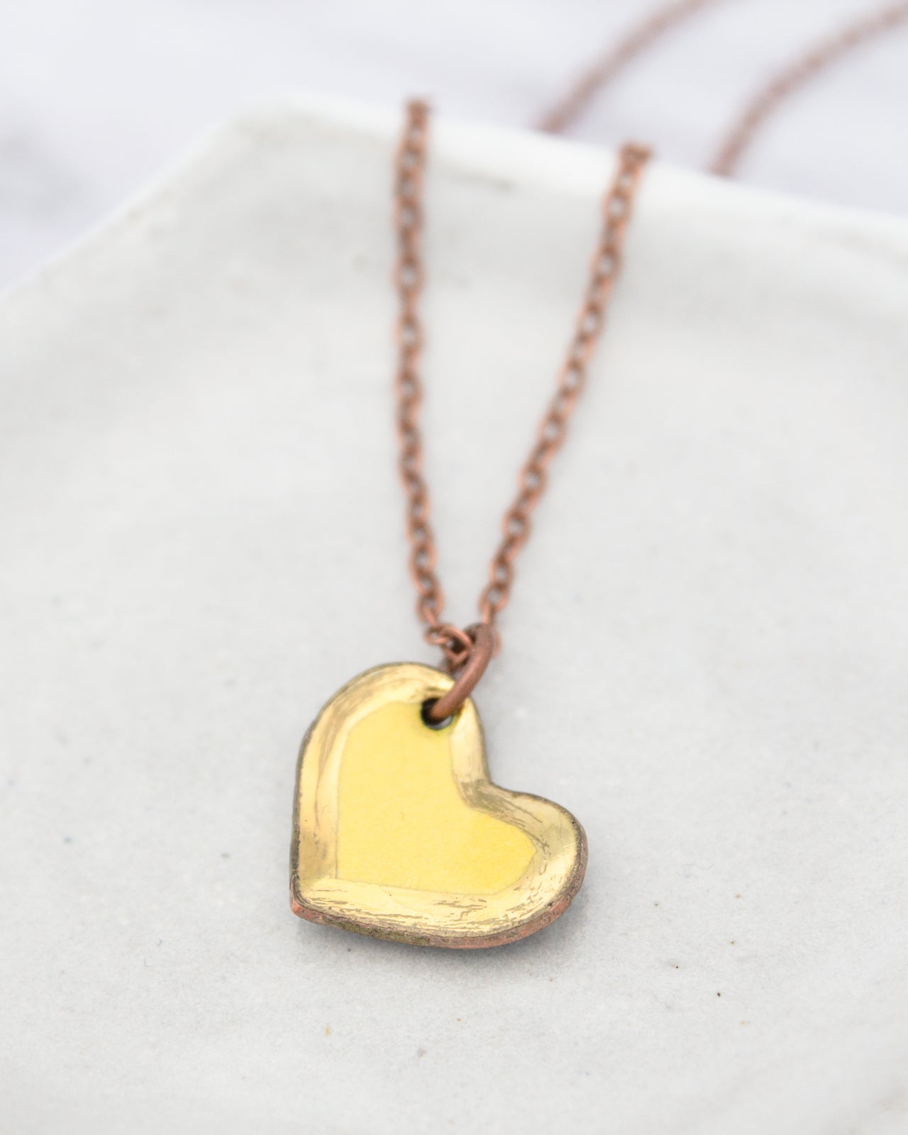 A delicate gold heart-shaped pendant necklace with a copper-colored chain is displayed against a white background.