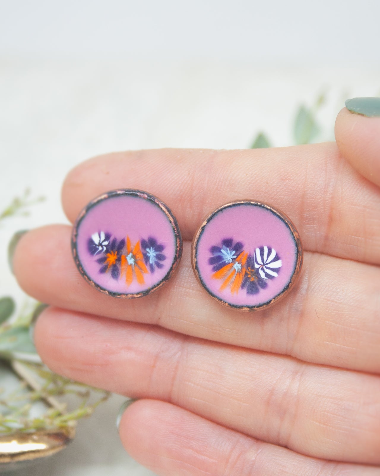A hand holding two circular earrings with colorful floral designs.