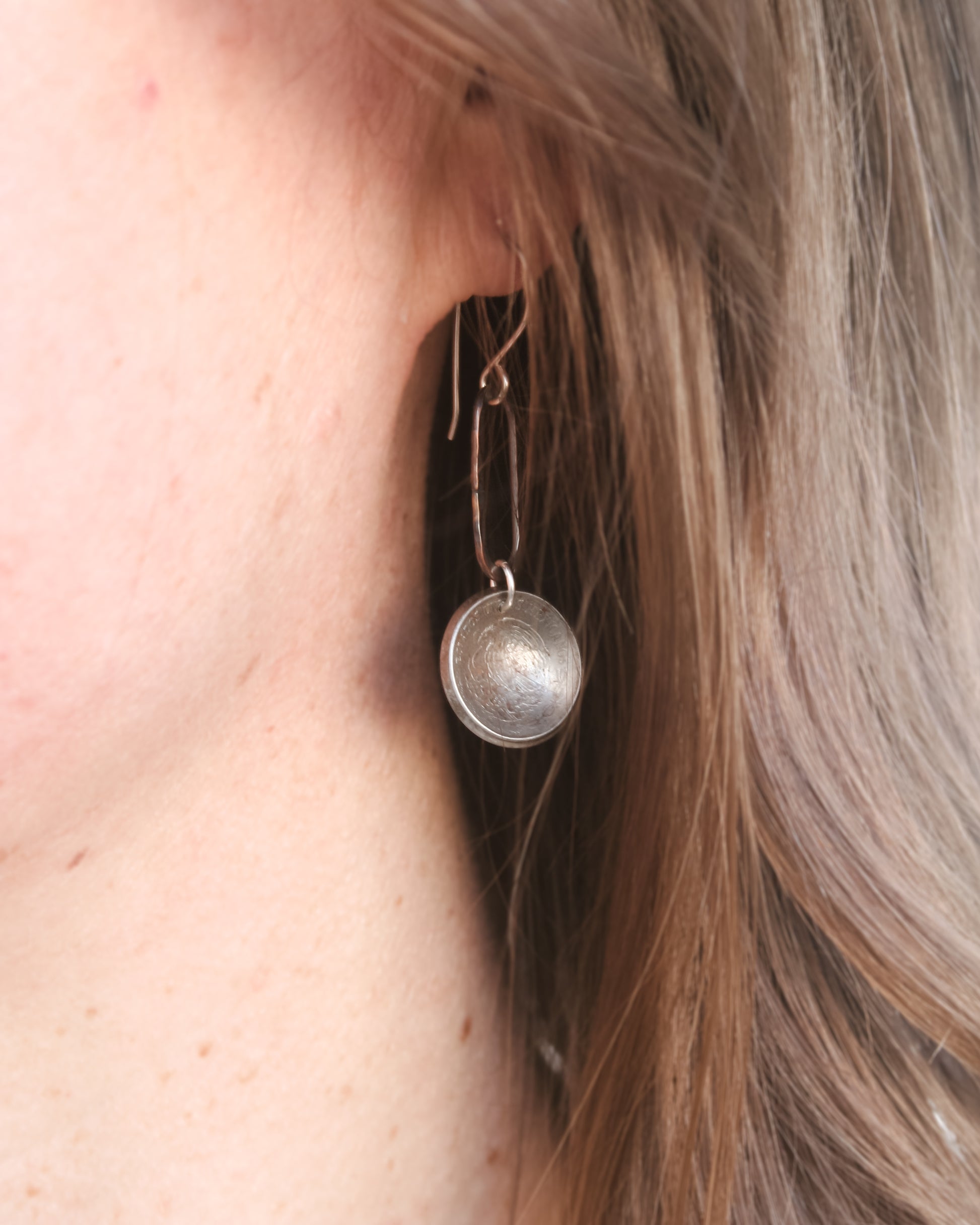 A close-up view of a person's ear with a silver earring featuring a circular design hanging from the earlobe.
