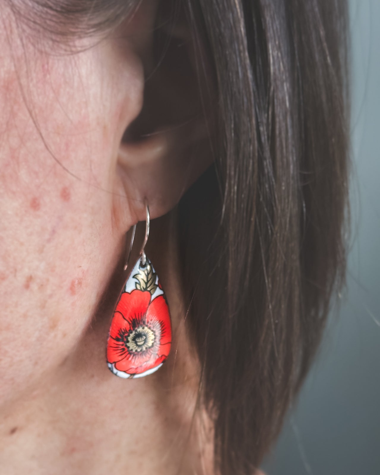 A close-up view of a person's ear wearing a red and white floral earring.