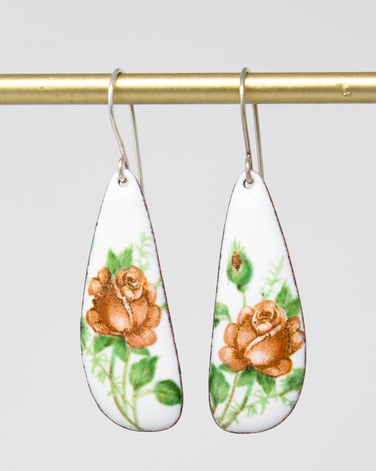 A pair of white earrings with floral designs, featuring orange roses and green leaves.