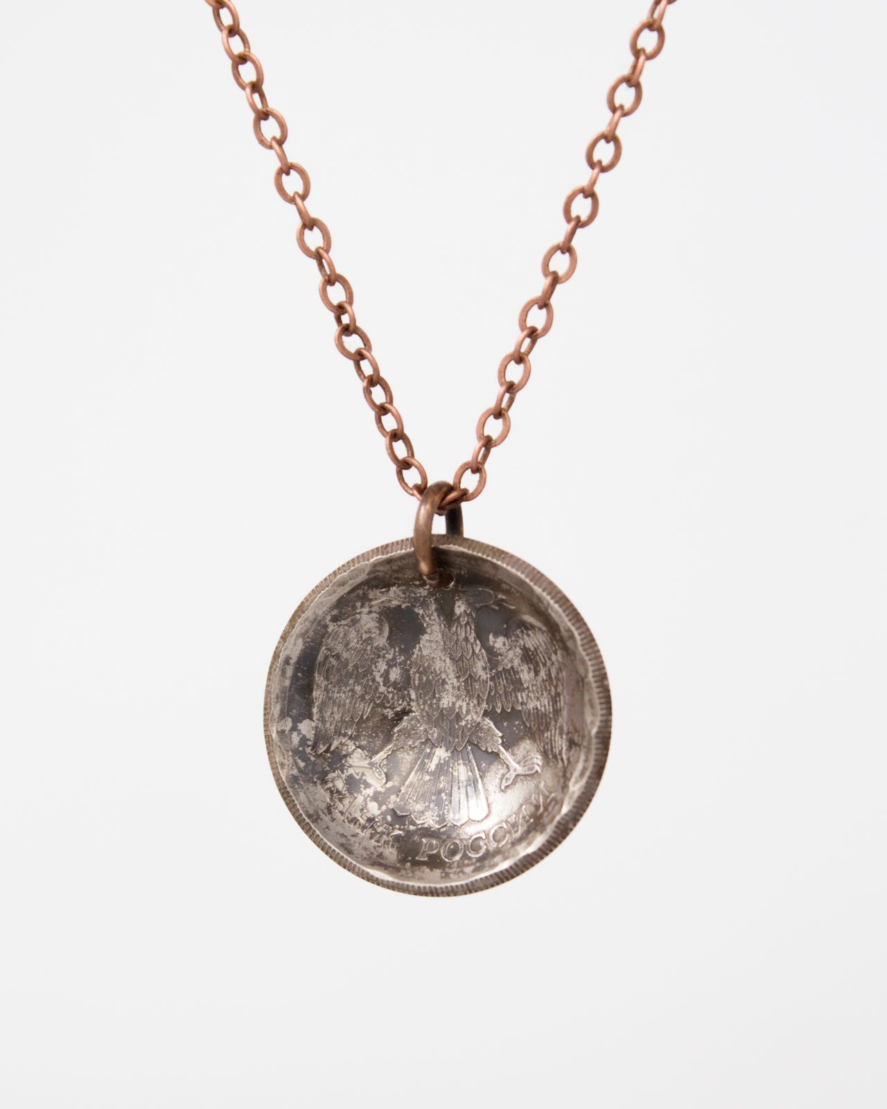 A silver-colored pendant necklace with a round, engraved design on the back.