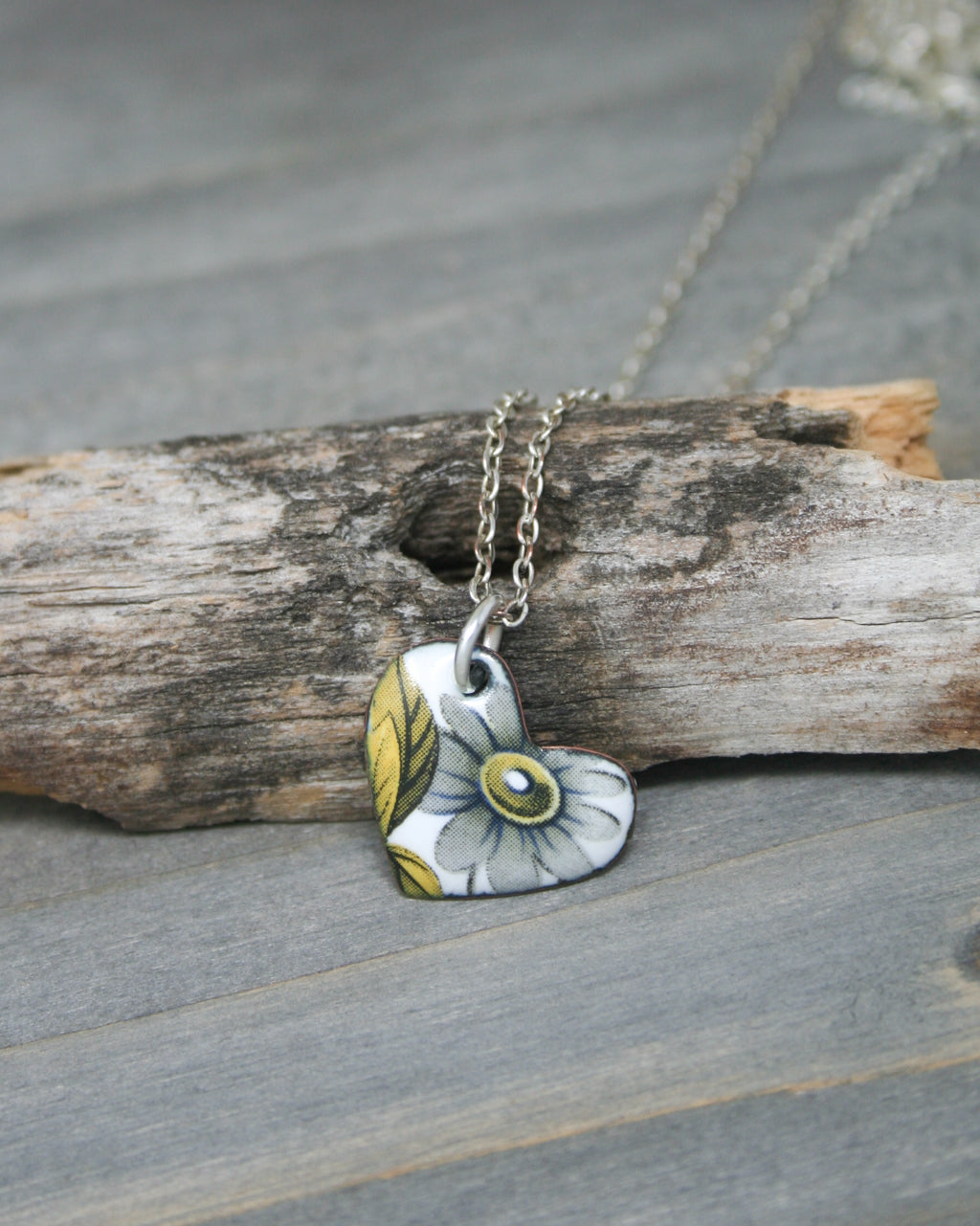 a necklace with a flower on it sitting on a piece of wood