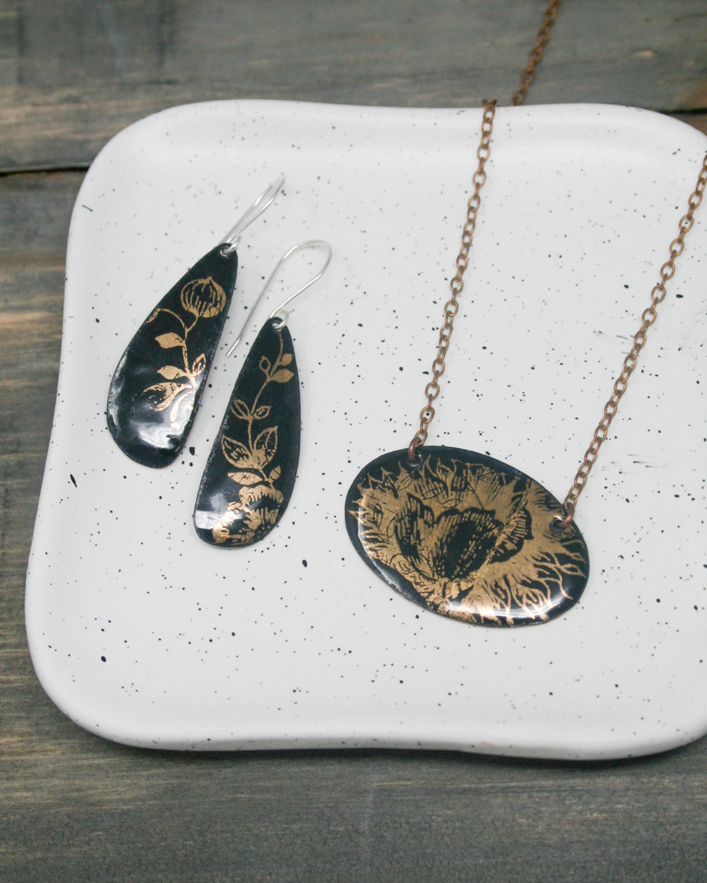 a pair of black earrings with gold floral designs and a necklace with a large oval pendant featuring a gold floral design.