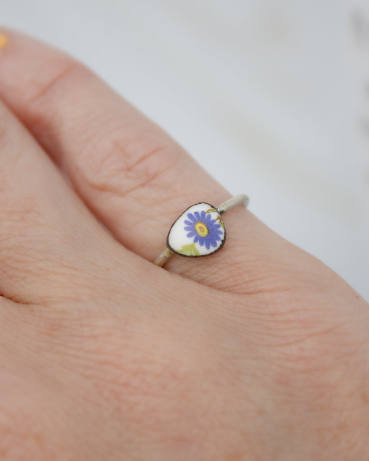 A close-up of a person's hand wearing a ring with a small, colorful flower design on it.