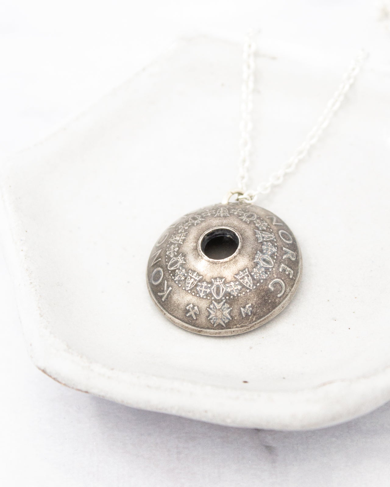 A silver necklace with a pendant is displayed on a white plate.