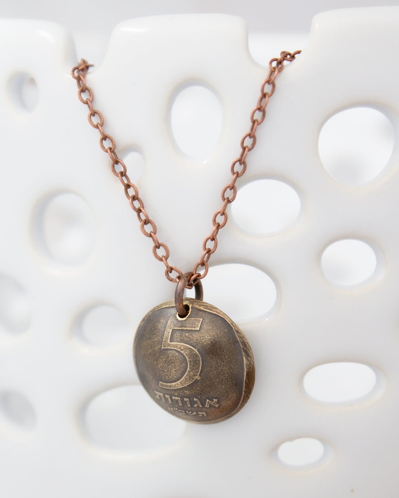 A necklace with a round pendant featuring the number 5 and some text on it, hanging against a white background.