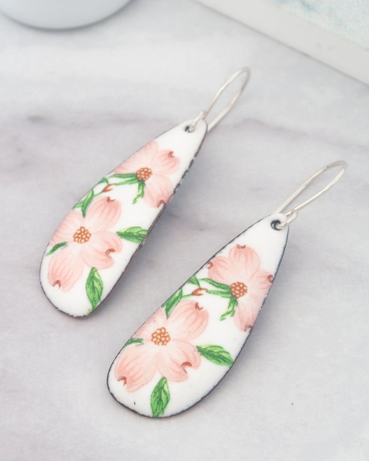 A pair of white earrings with pink flowers on a marble surface.
