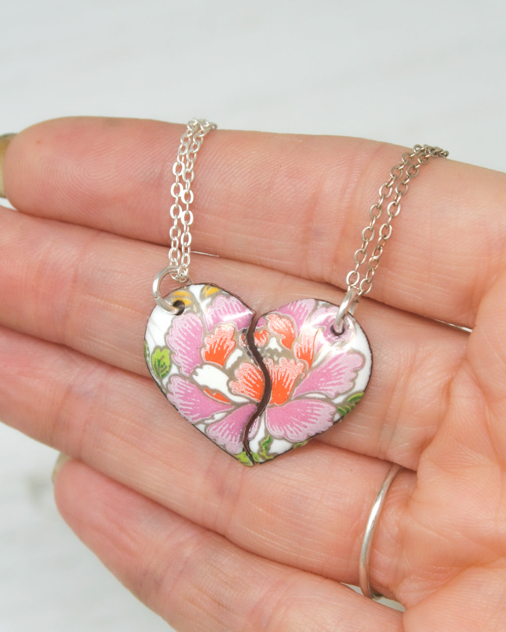A hand holding a heart-shaped pendant necklace with a floral design.