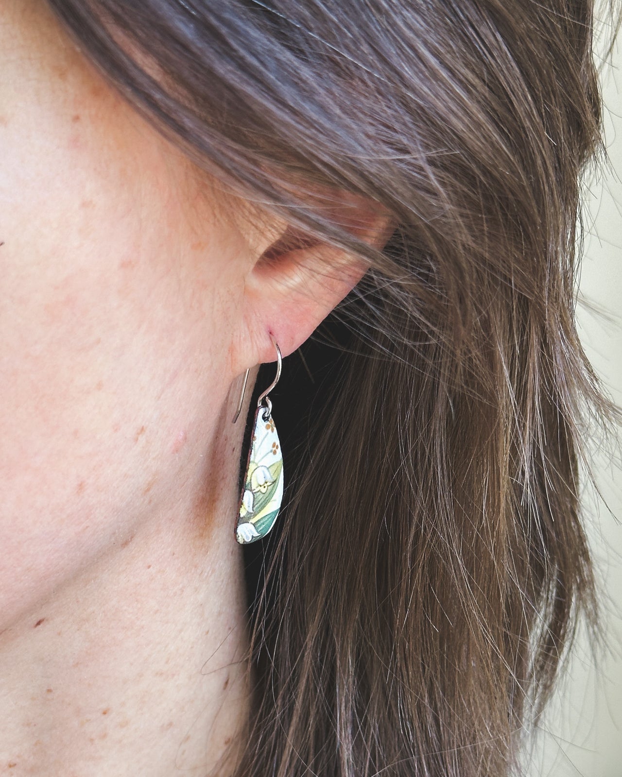 A close-up view of a person's ear with a floral earring hanging from it.