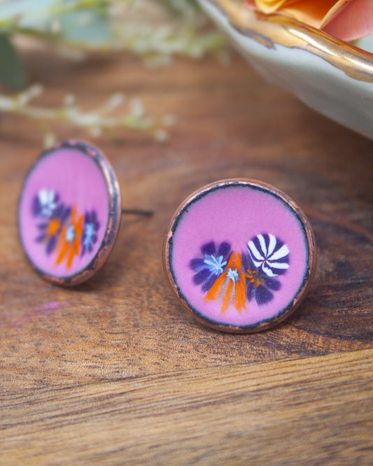 two round earrings with a floral design, placed on a wooden surface.