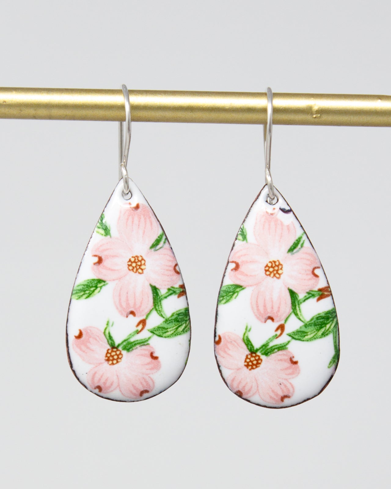 A pair of earrings with a floral design, featuring pink flowers and green leaves.