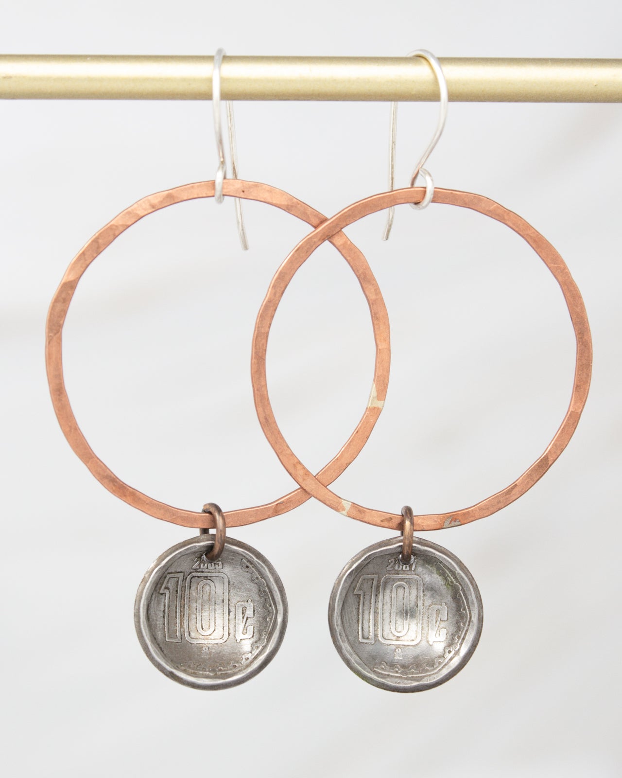A pair of earrings with a copper-colored metal ring and a silver-colored metal coin dangling from it.