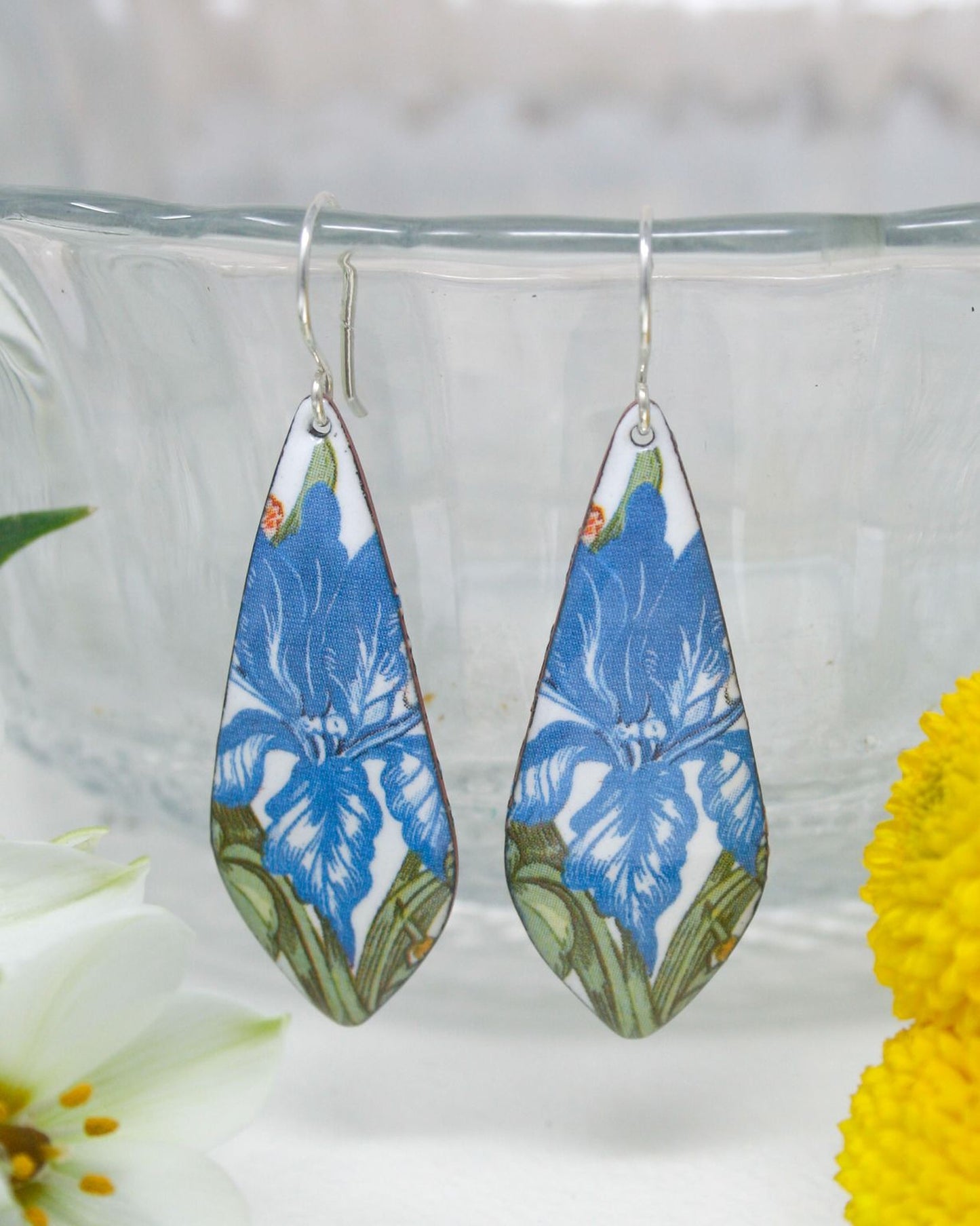 A pair of blue and white earrings with a floral pattern, hanging from a hook.