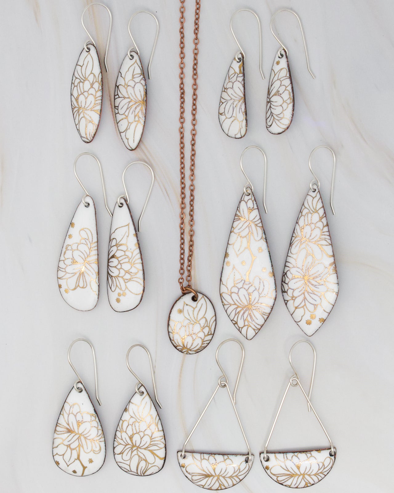 a collection of white and gold floral earrings and a necklace, arranged on a marble surface.