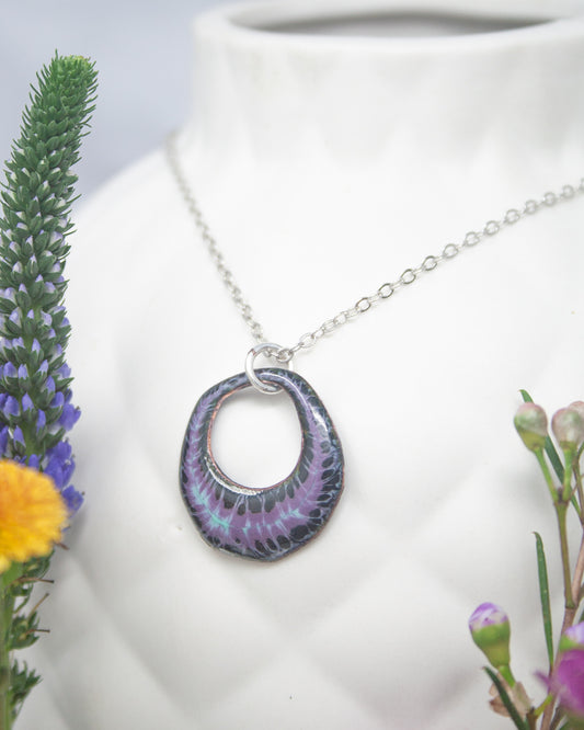 A necklace with a purple pendant is displayed against a white background, accompanied by a vase of colorful flowers.