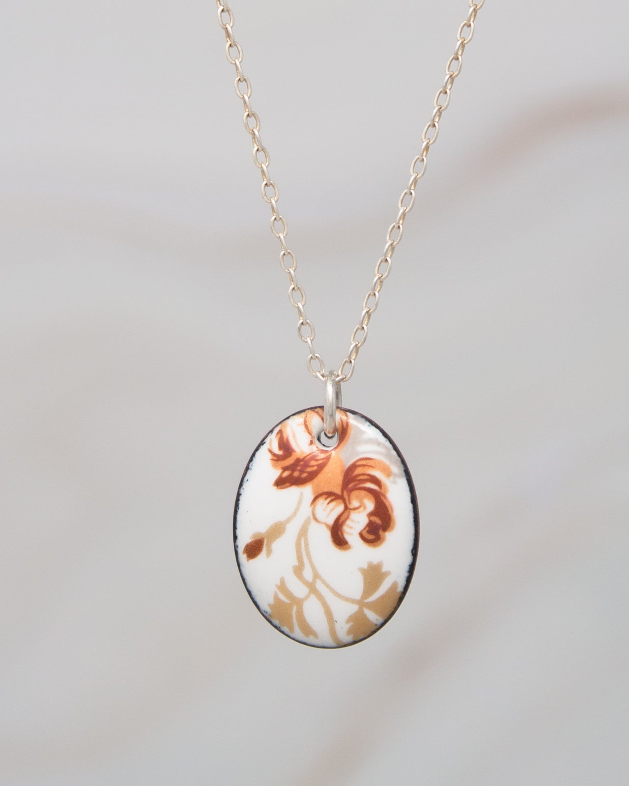 A delicate necklace with a pendant featuring a floral design in shades of brown and white.