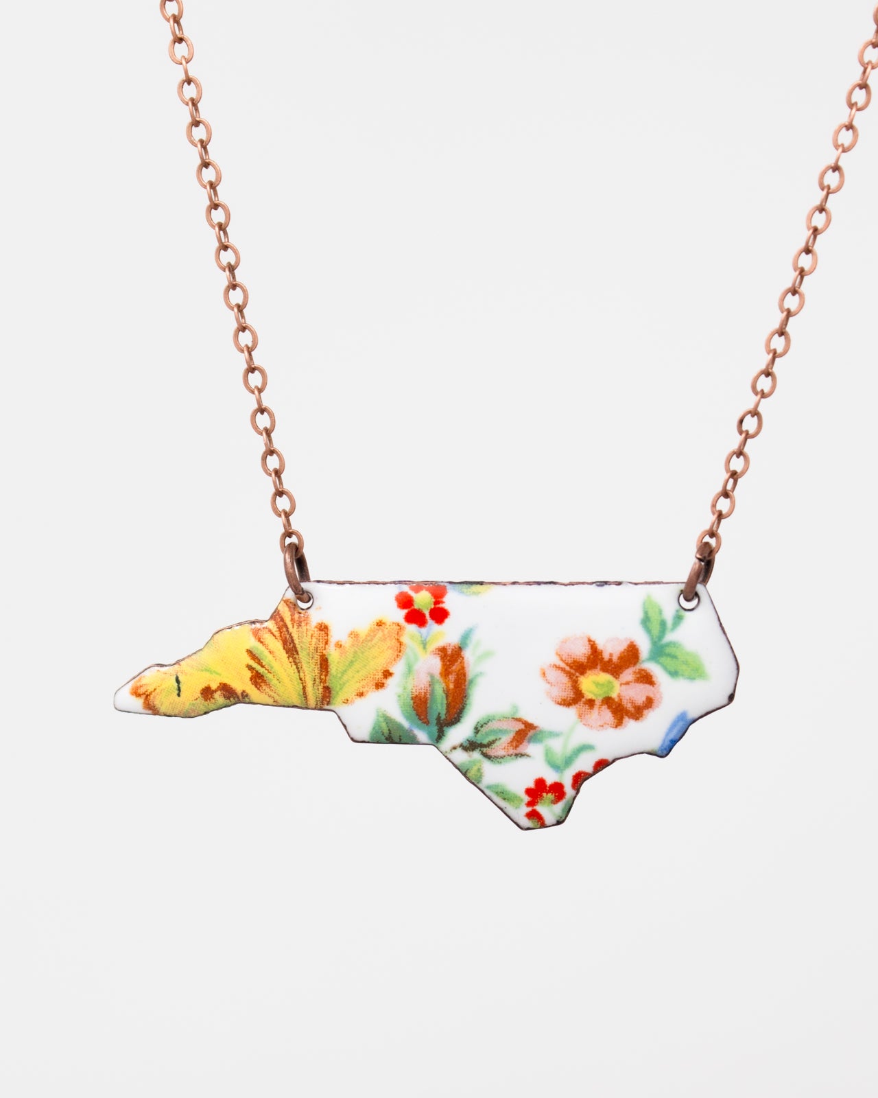 A necklace with a pendant in the shape of the state of North Carolina, featuring a floral design.