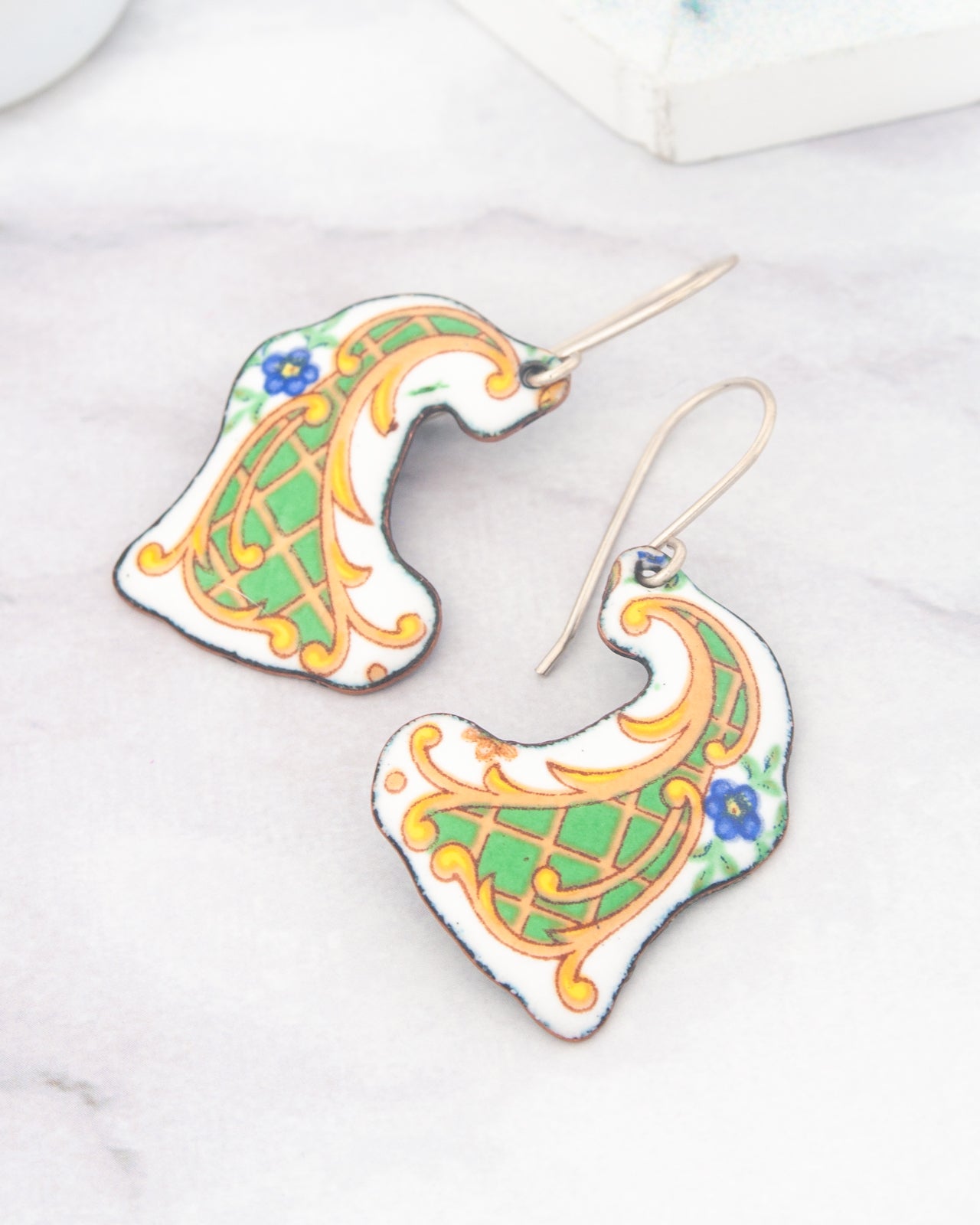 a pair of earrings with intricate designs, including floral and geometric patterns in shades of green, yellow, and blue.