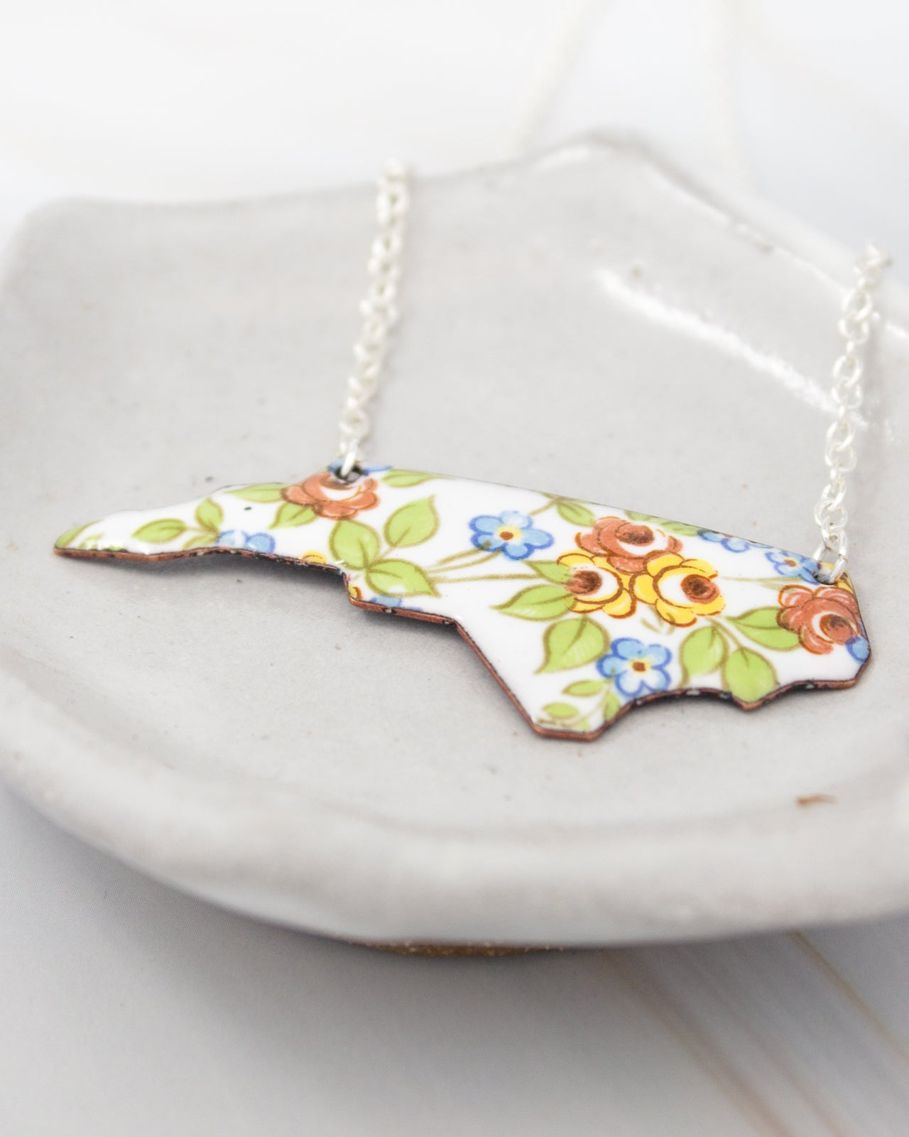 A necklace with a pendant in the shape of a flower design, featuring a combination of blue, orange, and green colors.