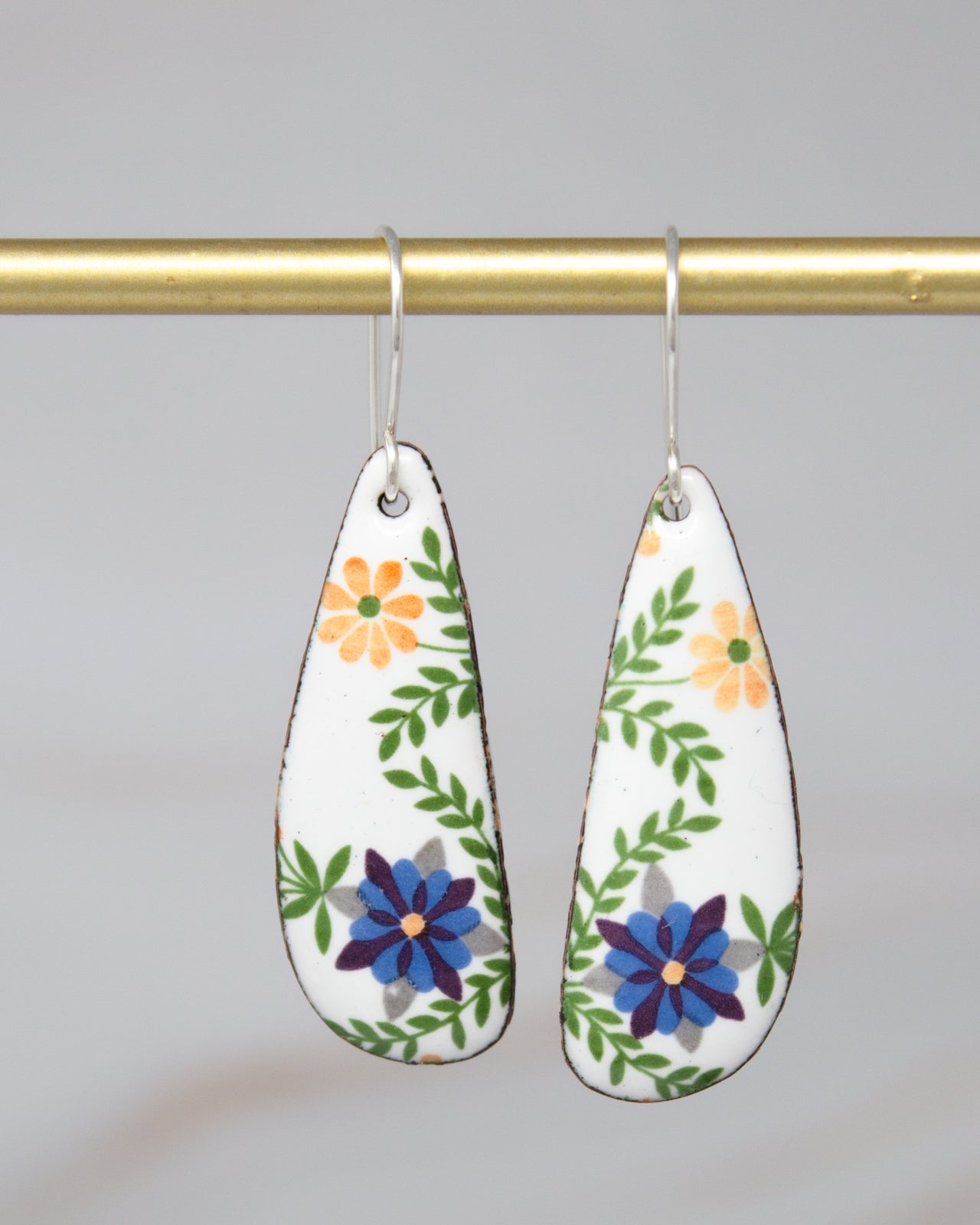 A pair of earrings with a floral design, featuring white and green flowers and leaves.