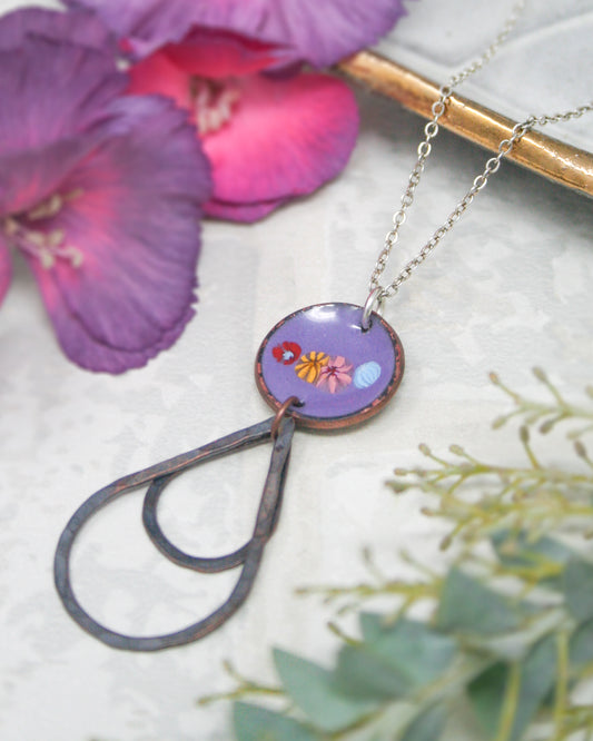a necklace with a purple pendant, resting on a white surface. The pendant is adorned with a floral design, adding a touch of elegance to the piece. The necklace is positioned in the center of the frame, drawing the viewer's attention to it. The background is blurred, keeping the focus on the necklace and its details.