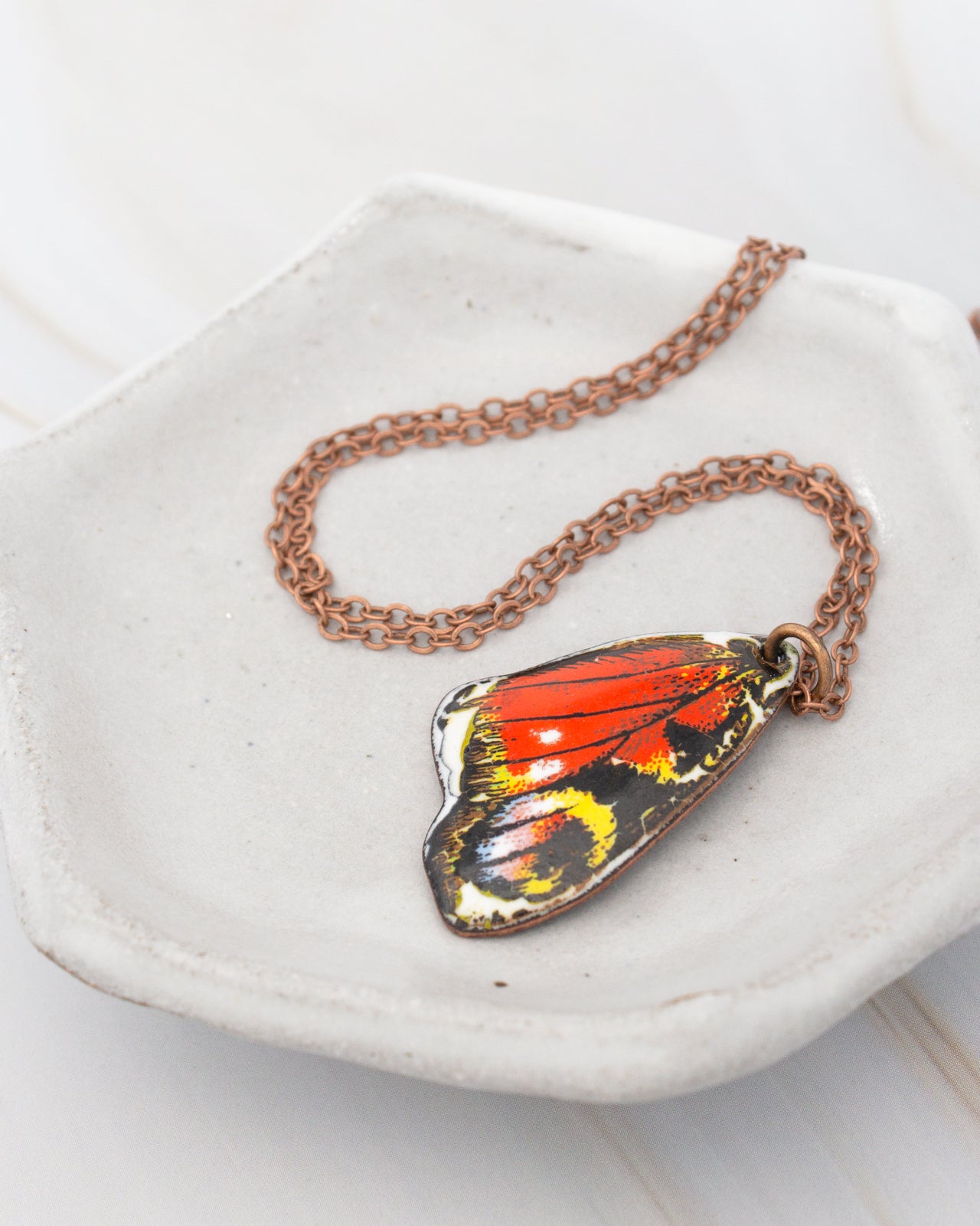 A necklace with a pendant in the shape of a colorful butterfly rests on a white plate.